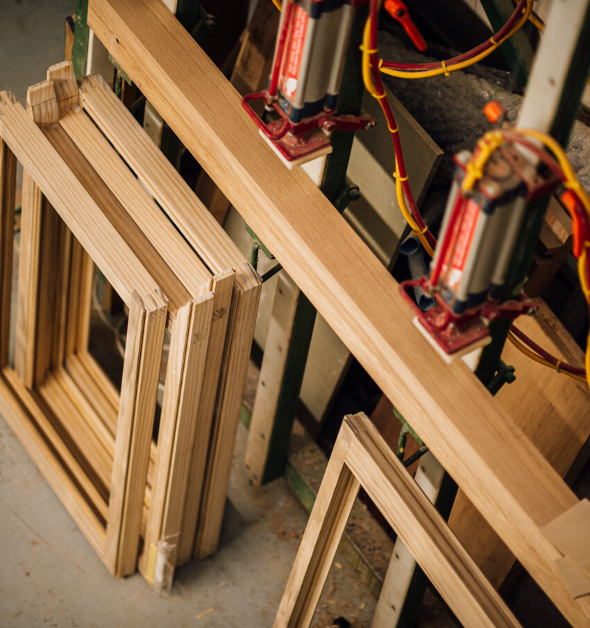 A series of timber window frames sit below a large woodworking machine in the Tucker Joinery workshop, Andover.