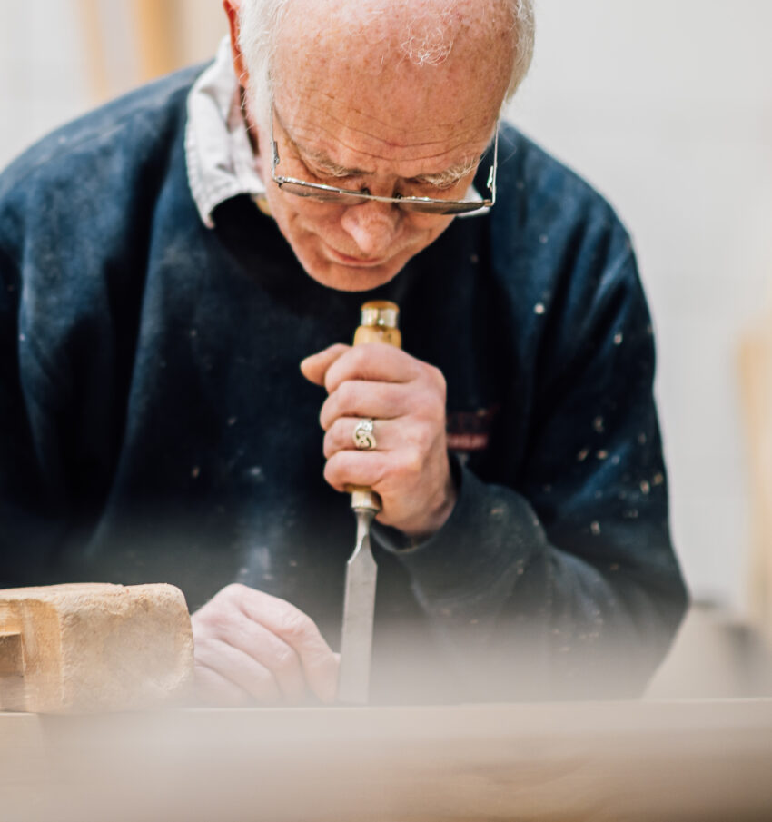 A member of the Tucker Joinery Team works on a piece of timber with a chisel. A wooden hammer sits next to him on the workbench in the Tucker Joinery workshop.