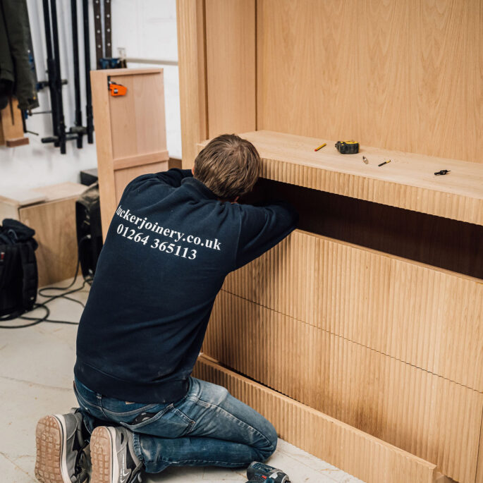 A woodworker wearing a Tucker Joinery branded sweatshirt works on the inner drawer of a bespoke, timber cabinet in the workshop.