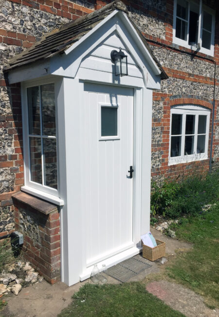 A white timber box door extension on a listed flint-stone building. Designed, built, finished and installed by tucker Joinery, Andover.