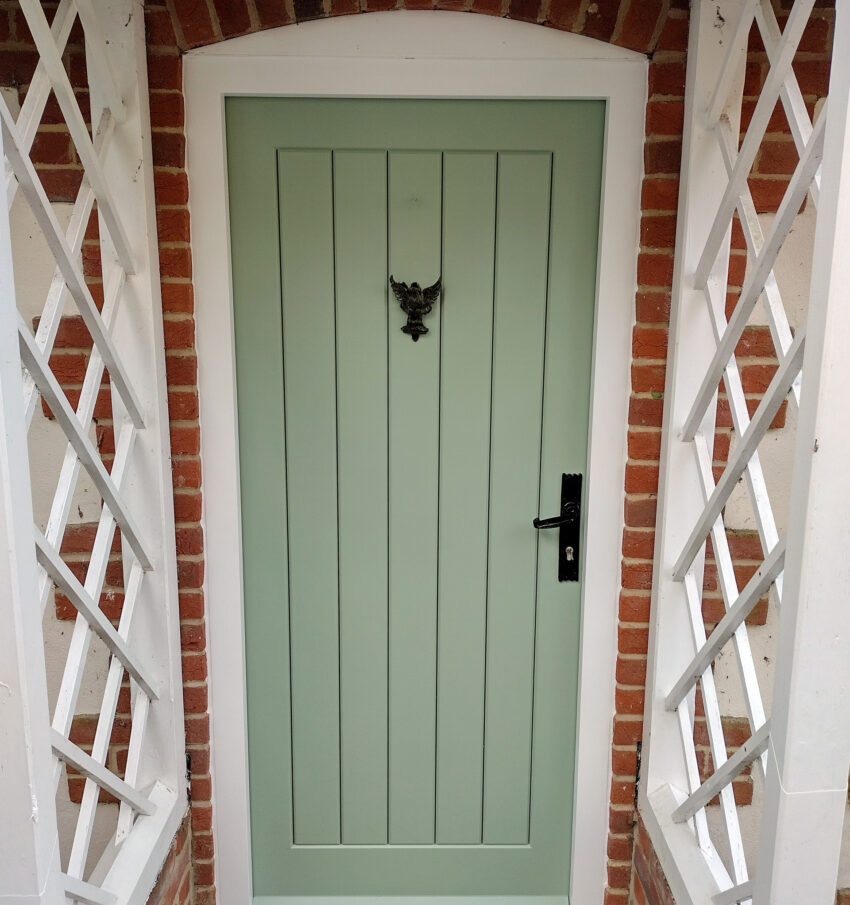 Hand-crafted wooden door, light green with a black iron handle and accents, designed, built, sprayed, finished, and fitted by Tucker Joinery based in Andover.