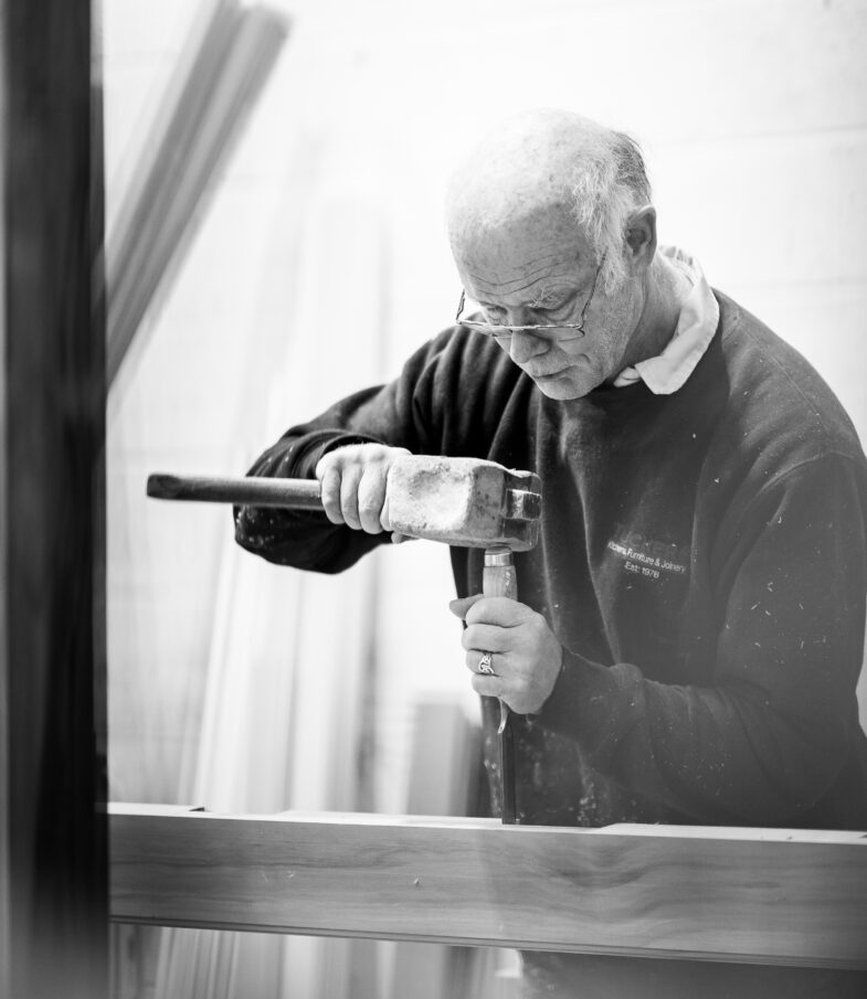 A member of the Tucker Joinery team carefully works the timber on his workbench with a mallet and chisel. Tucker Joinery workshop, Andover.