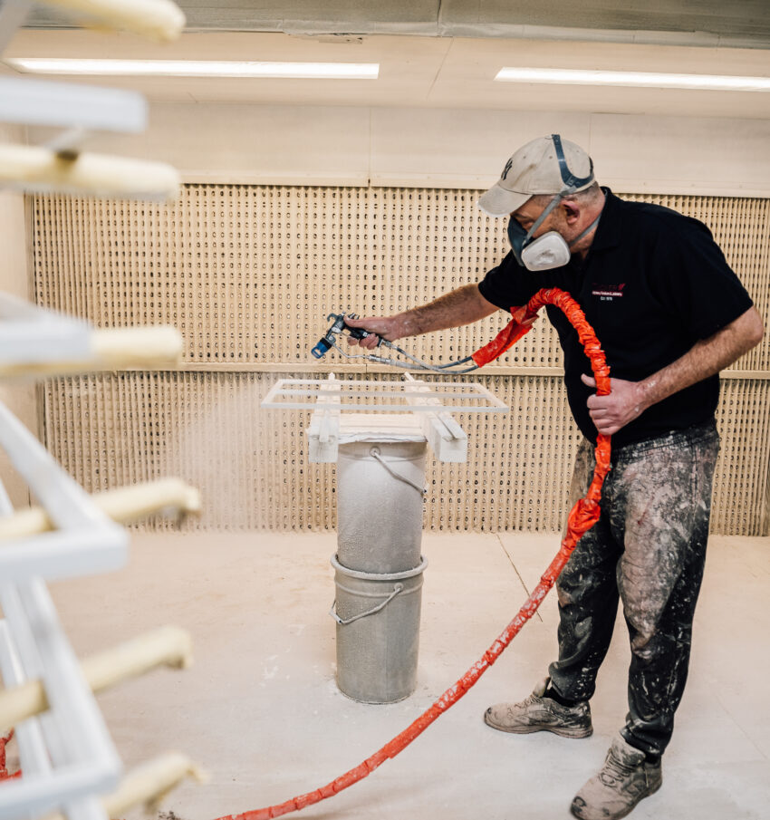 A member of the Tucker Joinery team (wearing appropriate safety gear) sprays timber frames white in the spray shop Tucker Joinery, based in Andover.