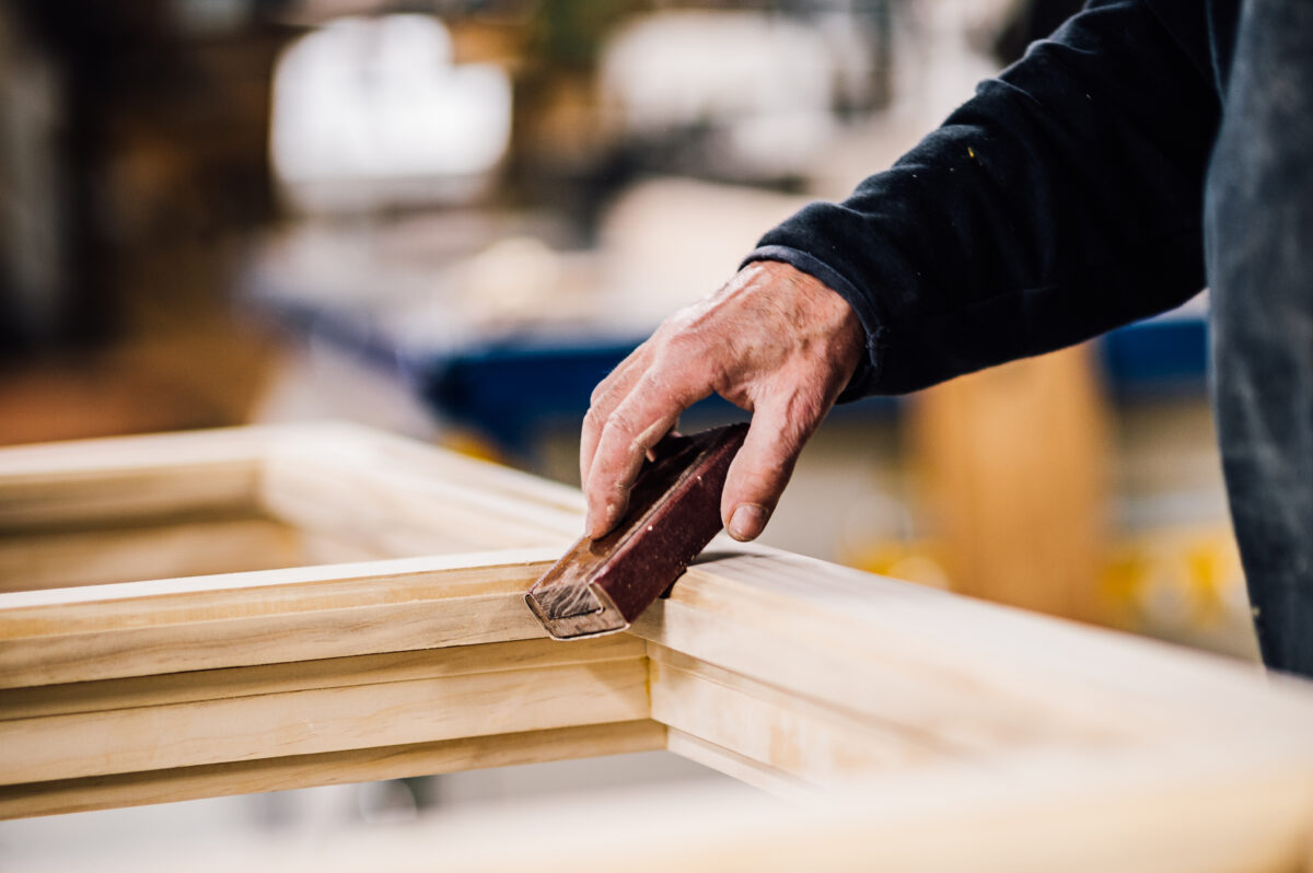 A member of the Tucker Joinery team sands the corners of a timber frame by hand, in the Tucker Joinery workshop.