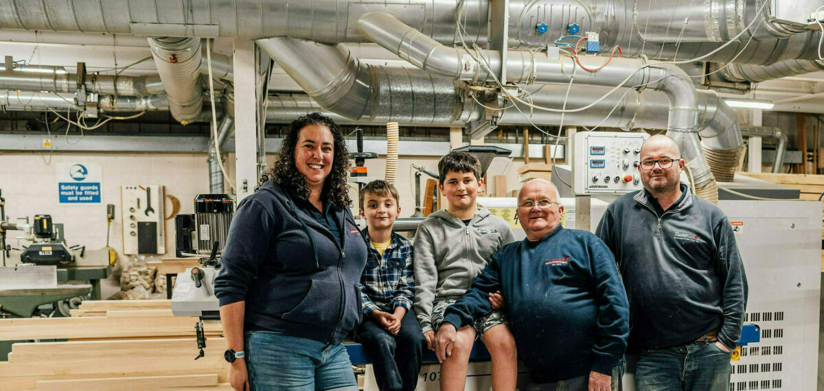 Three generations of the Tucker Family (Emma, Lee, Dave, Archie, and Ollie) sit together at the Tucker Joinery Workshop.