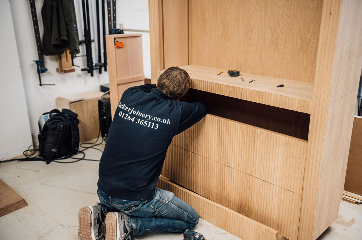 A woodworker wearing a Tucker Joinery branded sweatshirt works on the inner drawer of a bespoke, timber cabinet in the workshop.