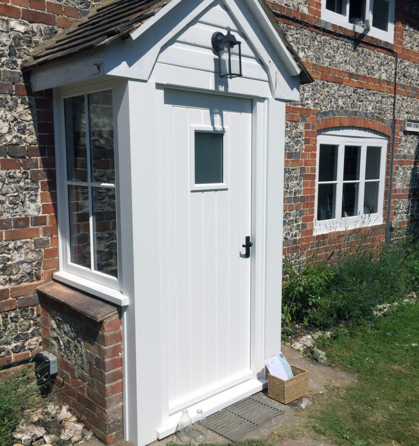 A white timber box door extension on a listed flint-stone building. Designed, built, finished and installed by tucker Joinery, Andover.